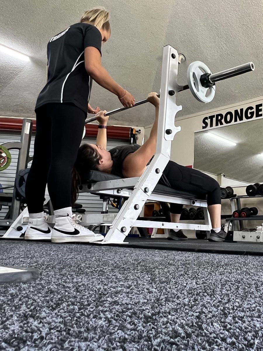 A person doing a bench press with a personal trainer in Otorohanga, New Zealand